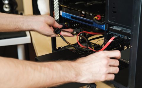 Young man repairs a computer system unit, changes parts, video card and hard drive, sets new components. Computer Repair Wizard.